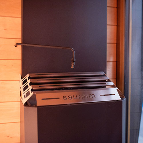 Saunum auto Leil water outlet installed above heater top, front close-up.