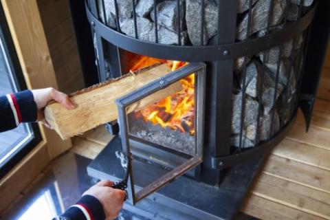 A person loading firewood into the open firebox of a Harvia Legend GreenFlame stove.