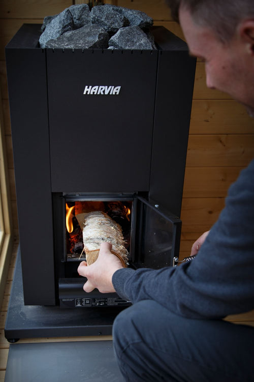A person loading wood into a Harvia Linear 18 Compact sauna stove.