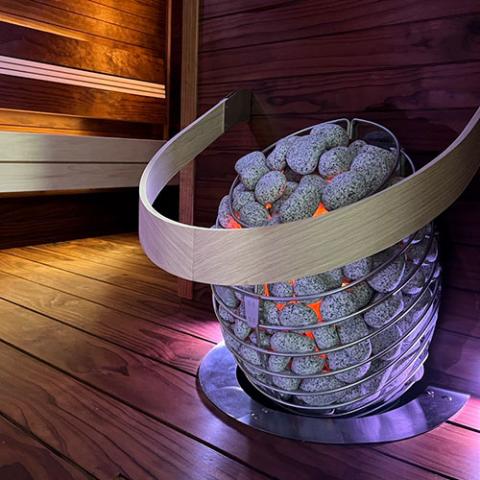 HUUM DROP stone-filled heater and wooden safety rail beside a sauna bench.