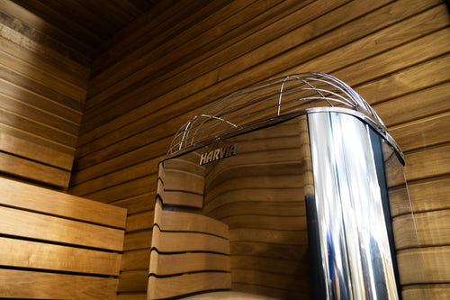 Low-angle view of the Harvia Club stainless-steel sauna heater beside wooden benches.