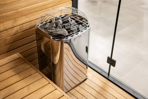 Harvia Club sauna heater beside wooden benches, elevated three-quarter view of stones and top guard.