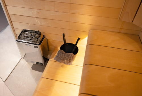Harvia KIP heater beside a wooden sauna bench with a black bucket and ladle.