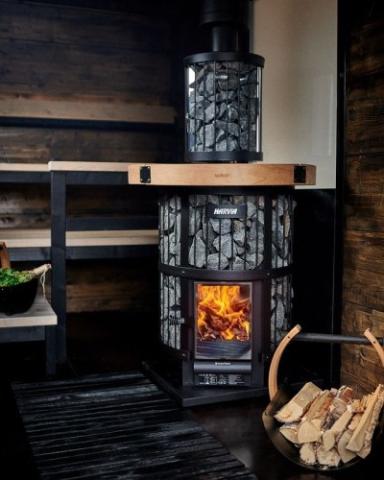 Harvia Legend GreenFlame stove and stone-filled chimney cover in a dark wood sauna.