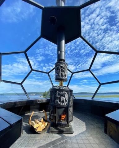 Harvia Legend GreenFlame stove inside a panoramic glass-walled sauna overlooking water.