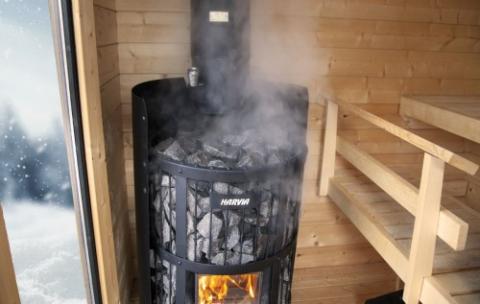 Steam rising from a Harvia Legend GreenFlame stove beside wooden sauna benches.