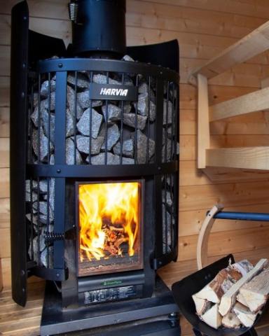 Harvia Legend GreenFlame stone-basket stove with a bright fire in a wood sauna.